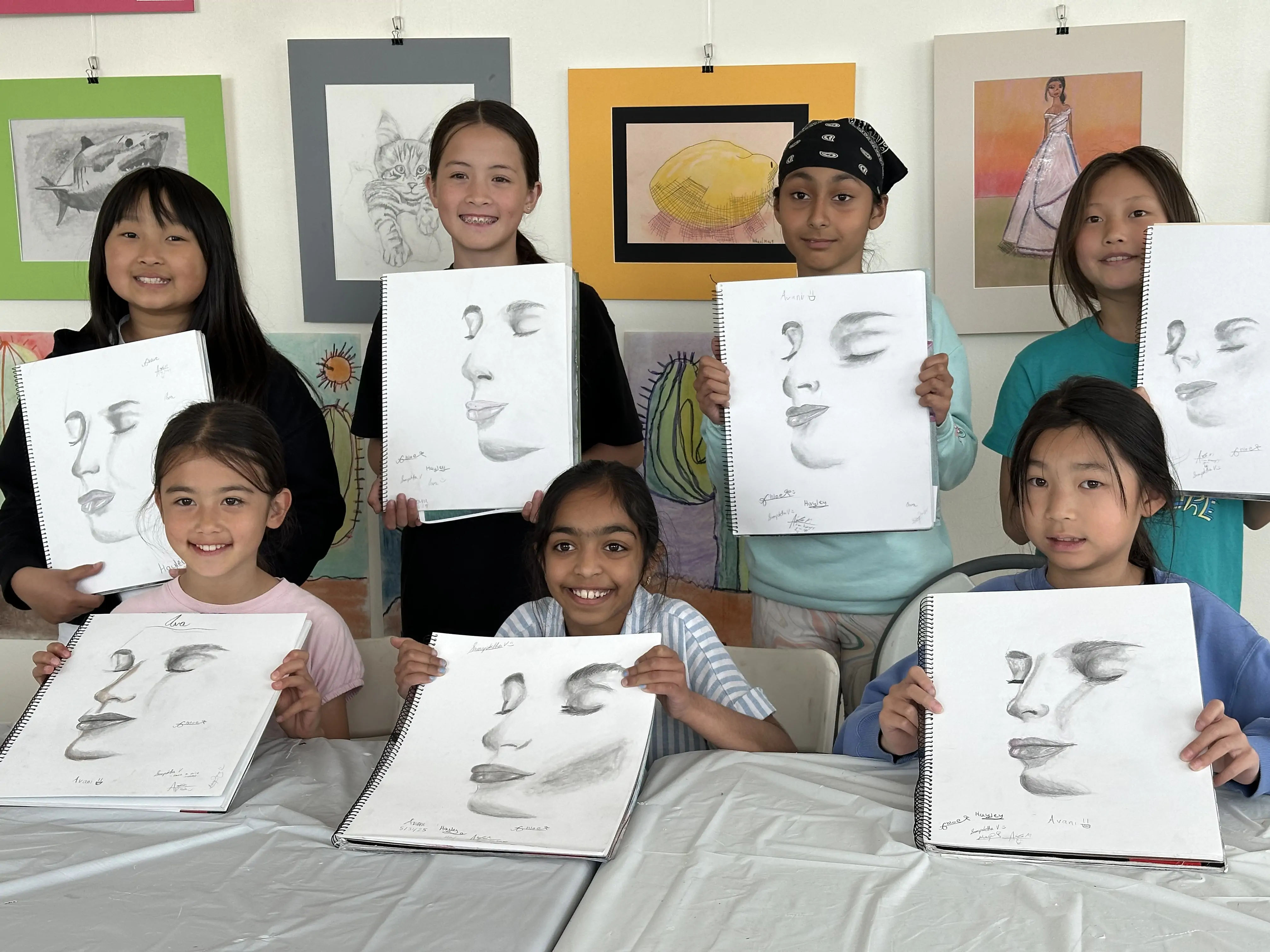 Group of young students proudly holding their graphite portrait drawings during an art class at Aliki’s Art House.